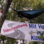 Drei Menschen in weißen Overalls besetzen Bäume. Auf einem Banner steht "Südschnellweg. Mit Vollgas in die Klimakrise"